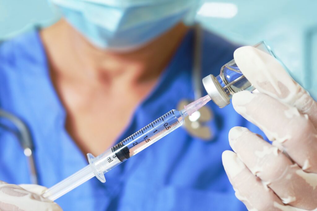 a person in a blue coat and gloves holding a syringe and a needle